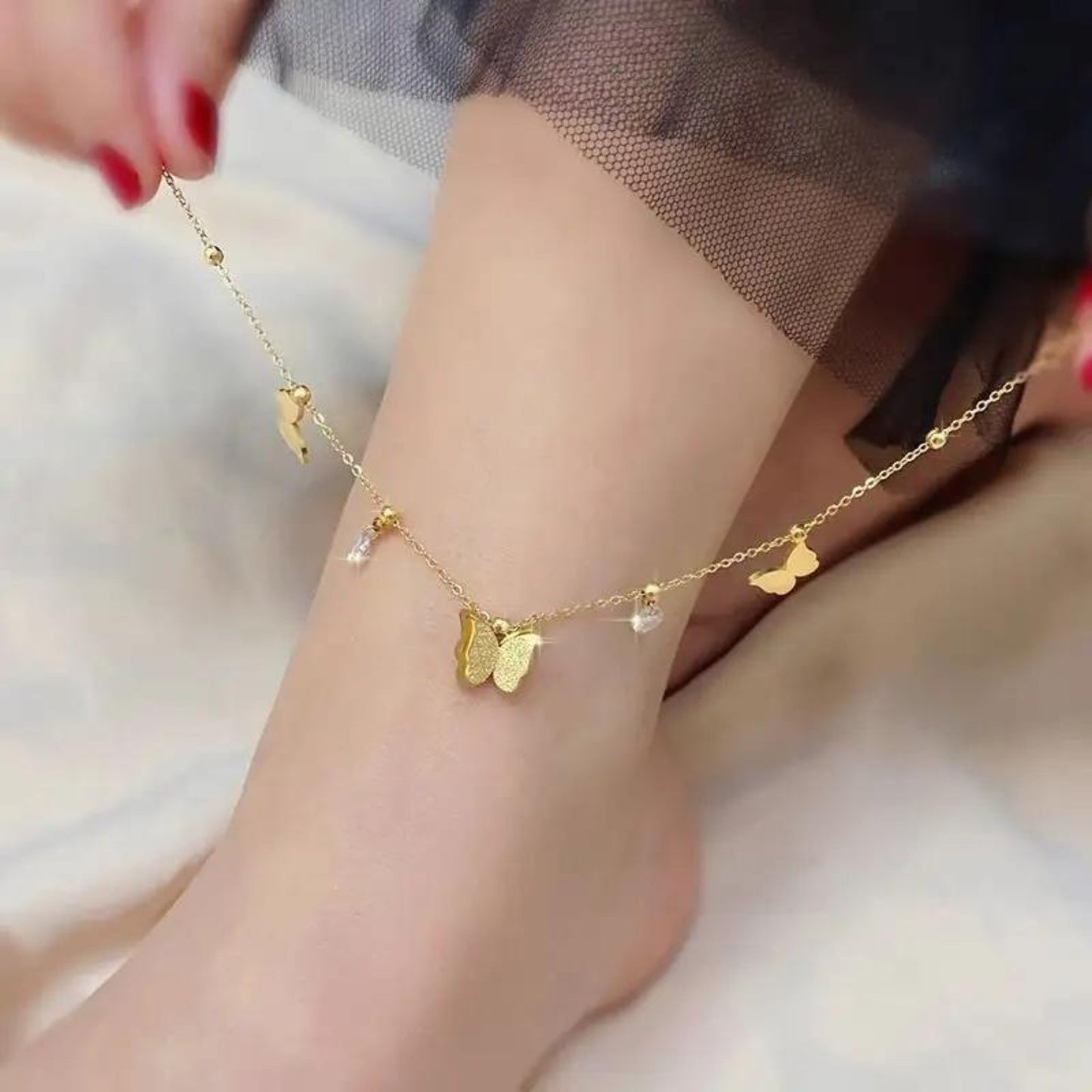 Butterfly Dreams Anklet styled on an ankle, showcasing its elegant butterfly charms and delicate crystal accents in 18K gold plating.