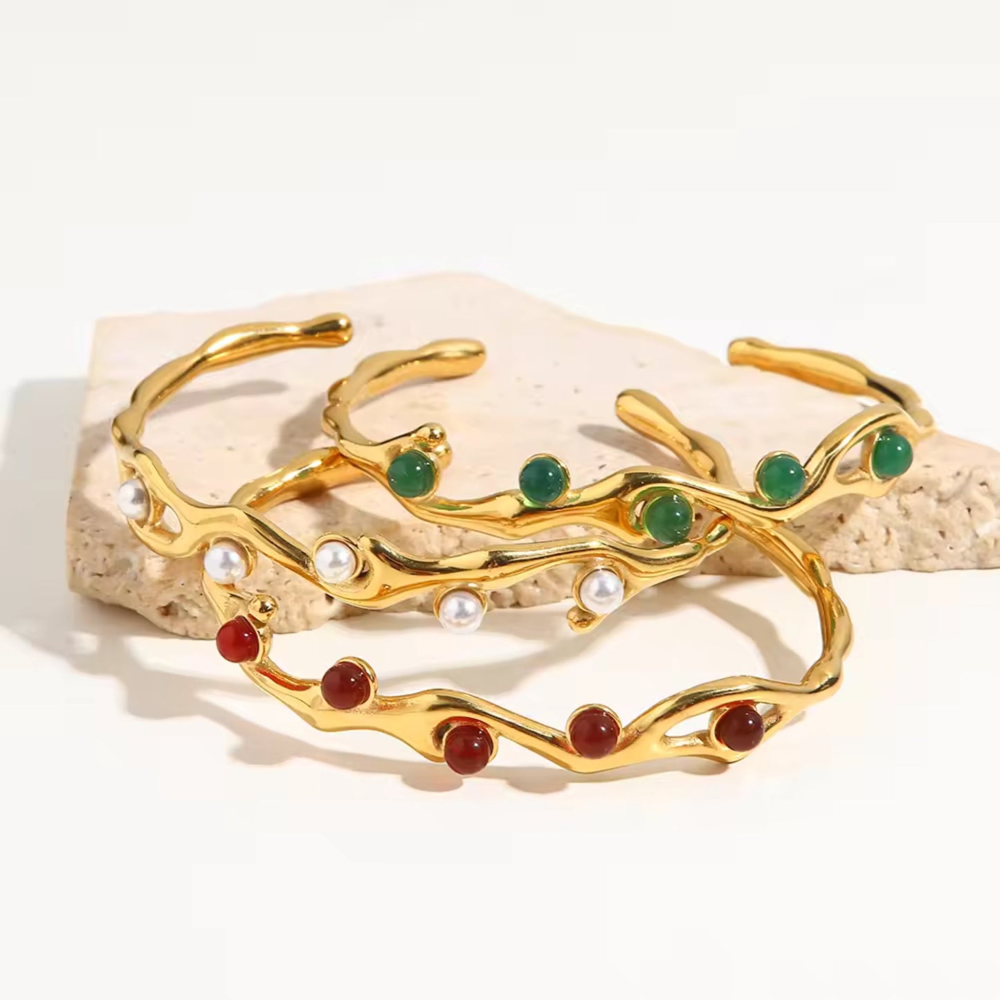Photo with background scene for the 
18K gold plated adjustable vine bangle bracelet with a choice of freshwater pearl, green gemstone, or red gemstone, featuring a delicate vine design and durable stainless steel construction