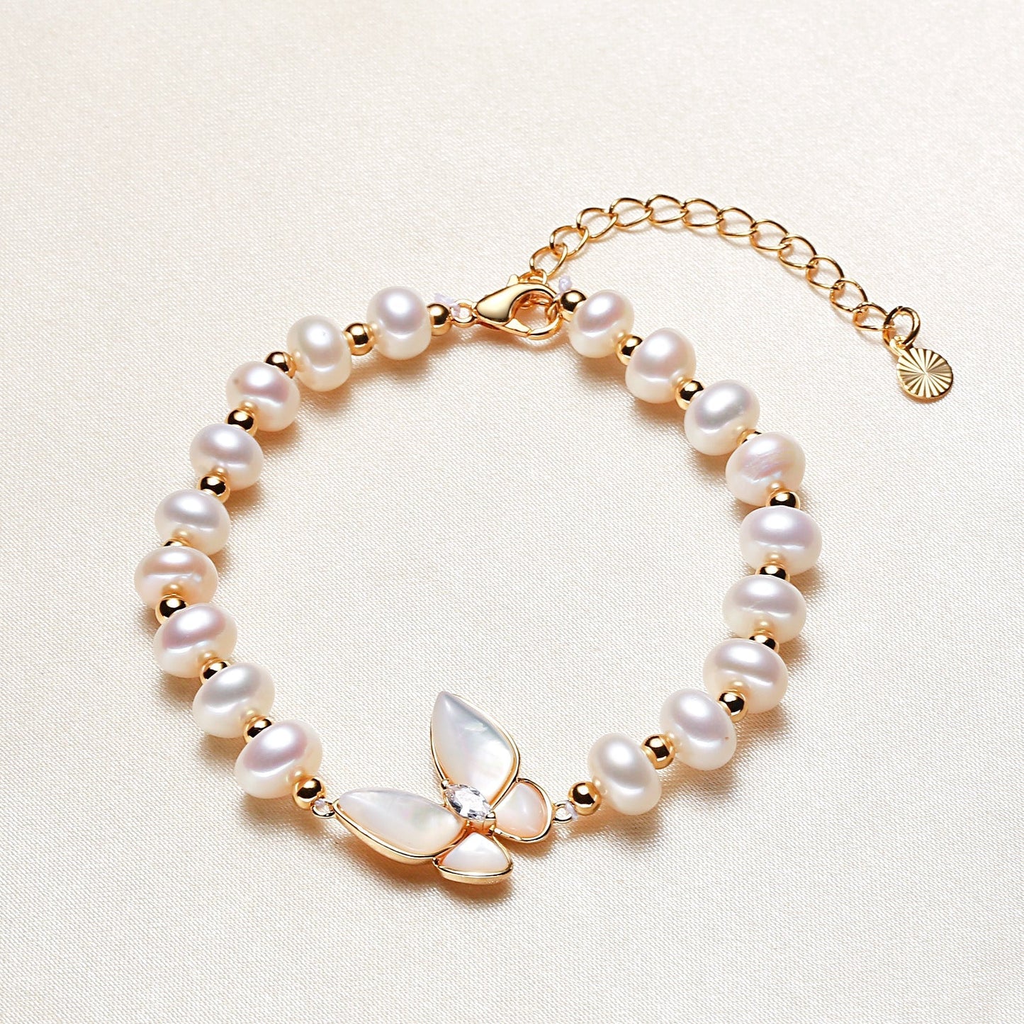 Butterfly Bliss Bracelet featuring 14K gold plating, freshwater pearl, & a mother-of-pearl butterfly charm, styled on a table