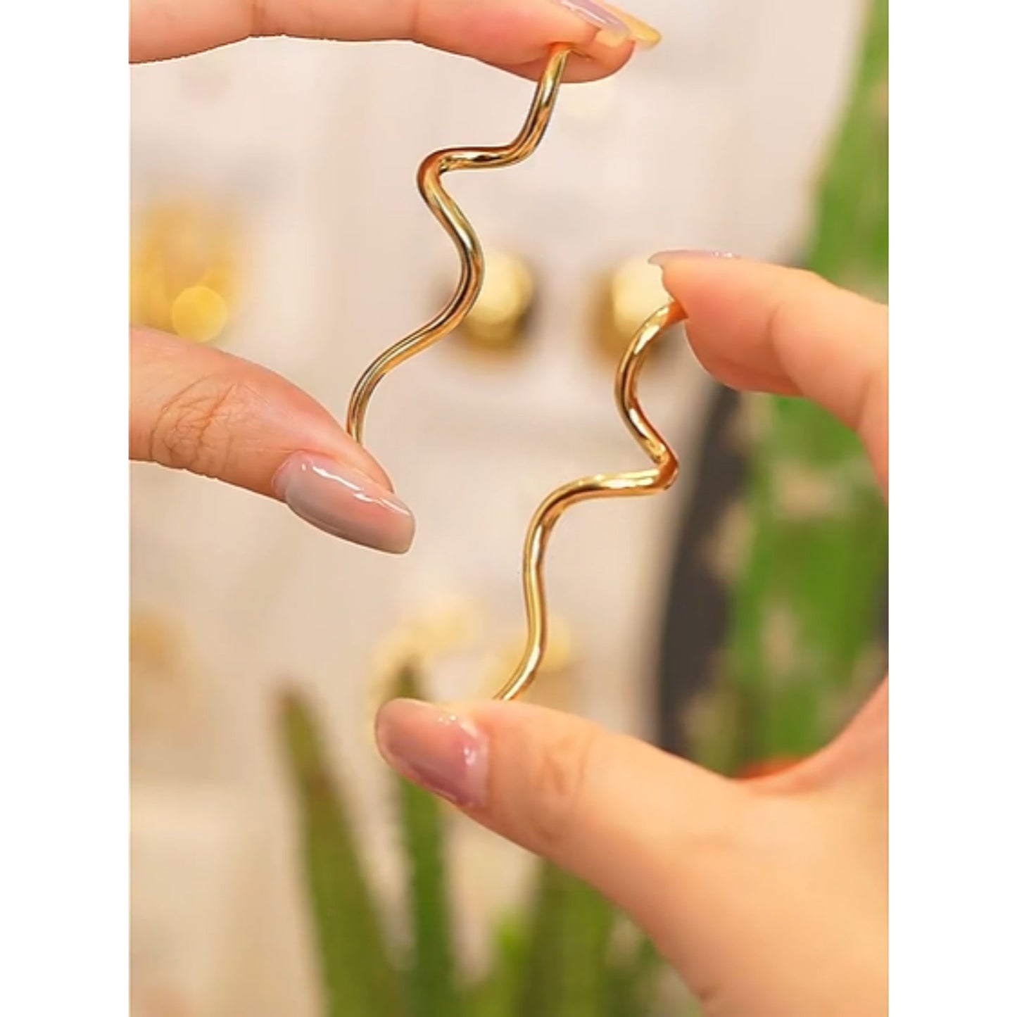 Model holding the Curved Minimalist Gold Drop Earrings, highlighting their sleek silhouette.