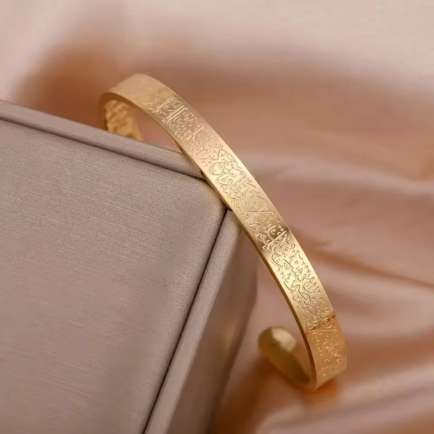 Divine Radiance Al Kursi Bangle with 18K gold plating and intricate Quranic verse engraving, displayed elegantly.