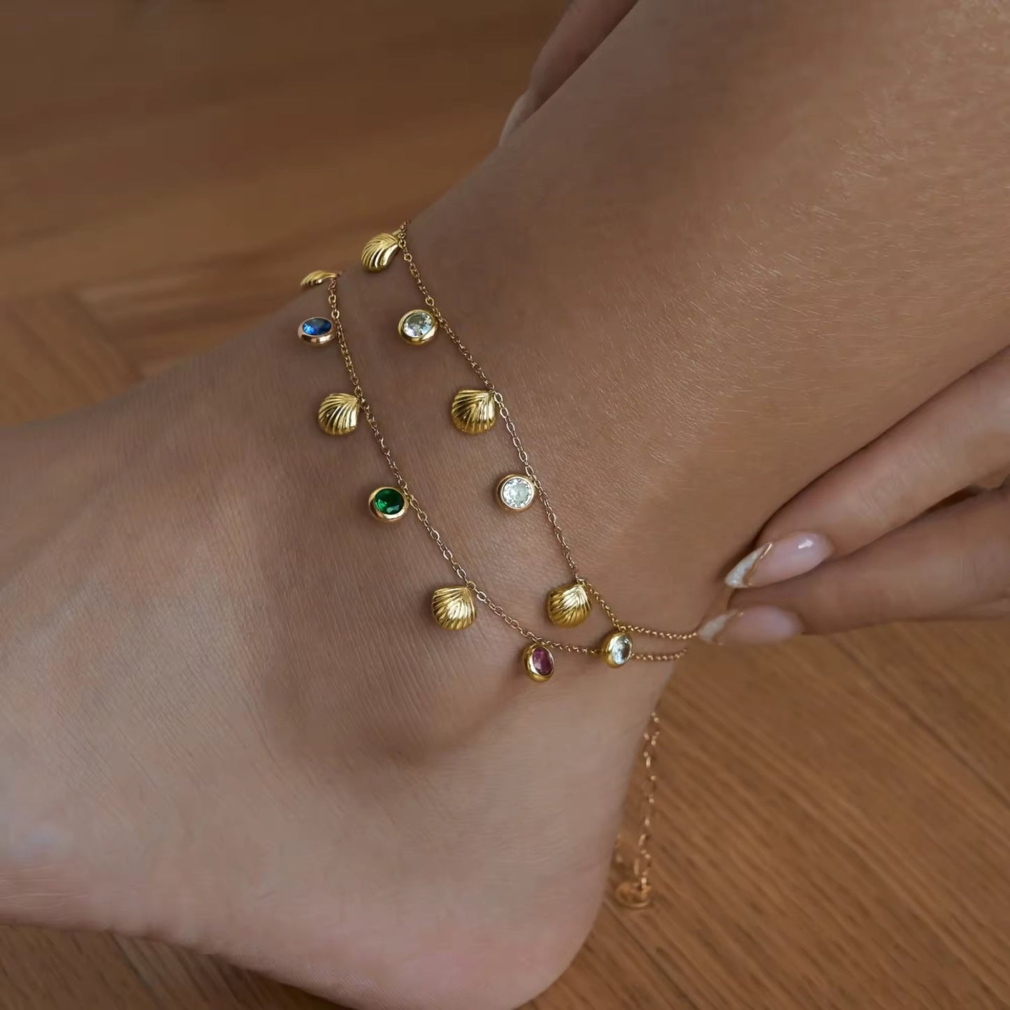 Model displaying a playful 18K gold-plated seashell anklet with multicolored and white zircon stones, adding a chic touch to a summery outfit.
