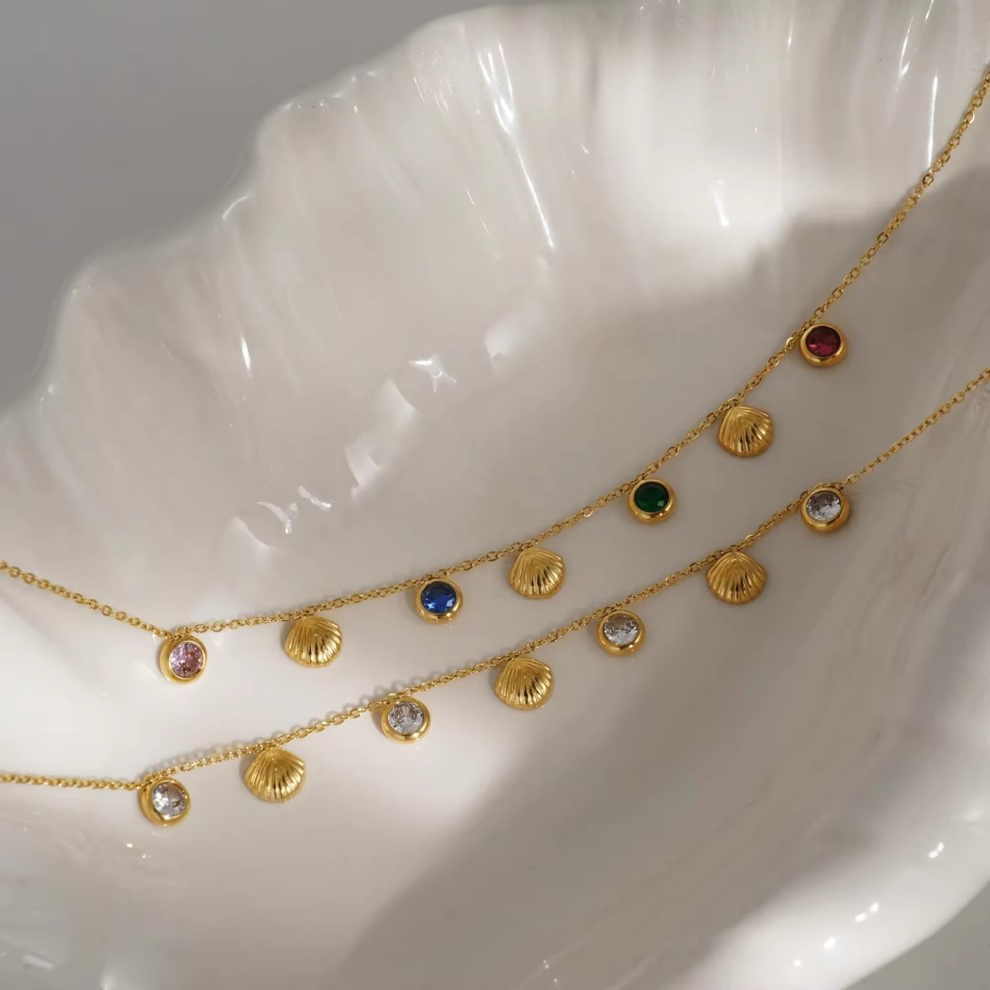 Side-by-side view of 18K gold-plated seashell anklets, one with radiant white zircons and the other with multicolored zircons, laid out stylishly for comparison.