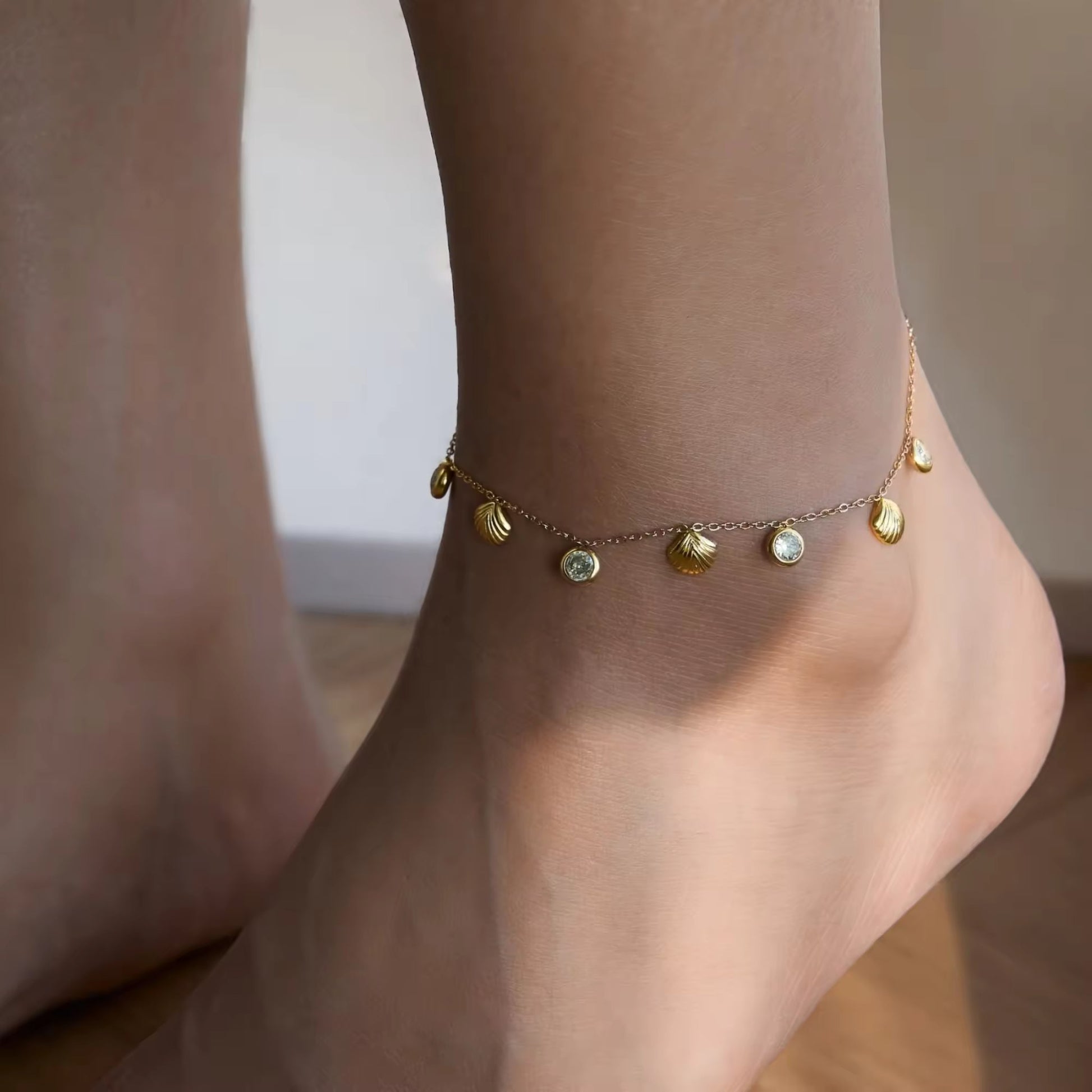 Model wearing an elegant 18K gold-plated seashell anklet with white zircons, styled for a beach outing or casual summer day.