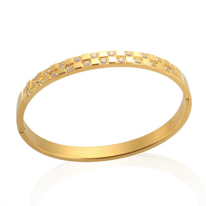 Close-up of a gold-plated stainless steel cuff bracelet with a checkered pattern of cubic zirconia stones, displayed on a white background.