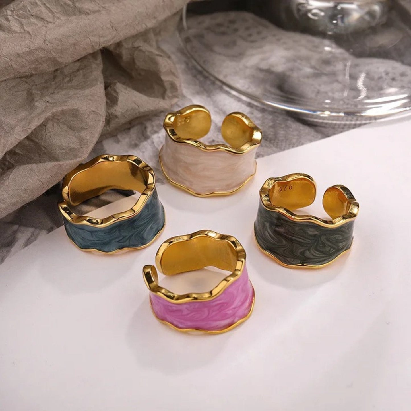 Set of Enchanted Wave Adjustable Rings in White, Purple, Dark Blue, and Dark Gray enamel, showcasing their elegant wave design and 18K gold-plated finish.