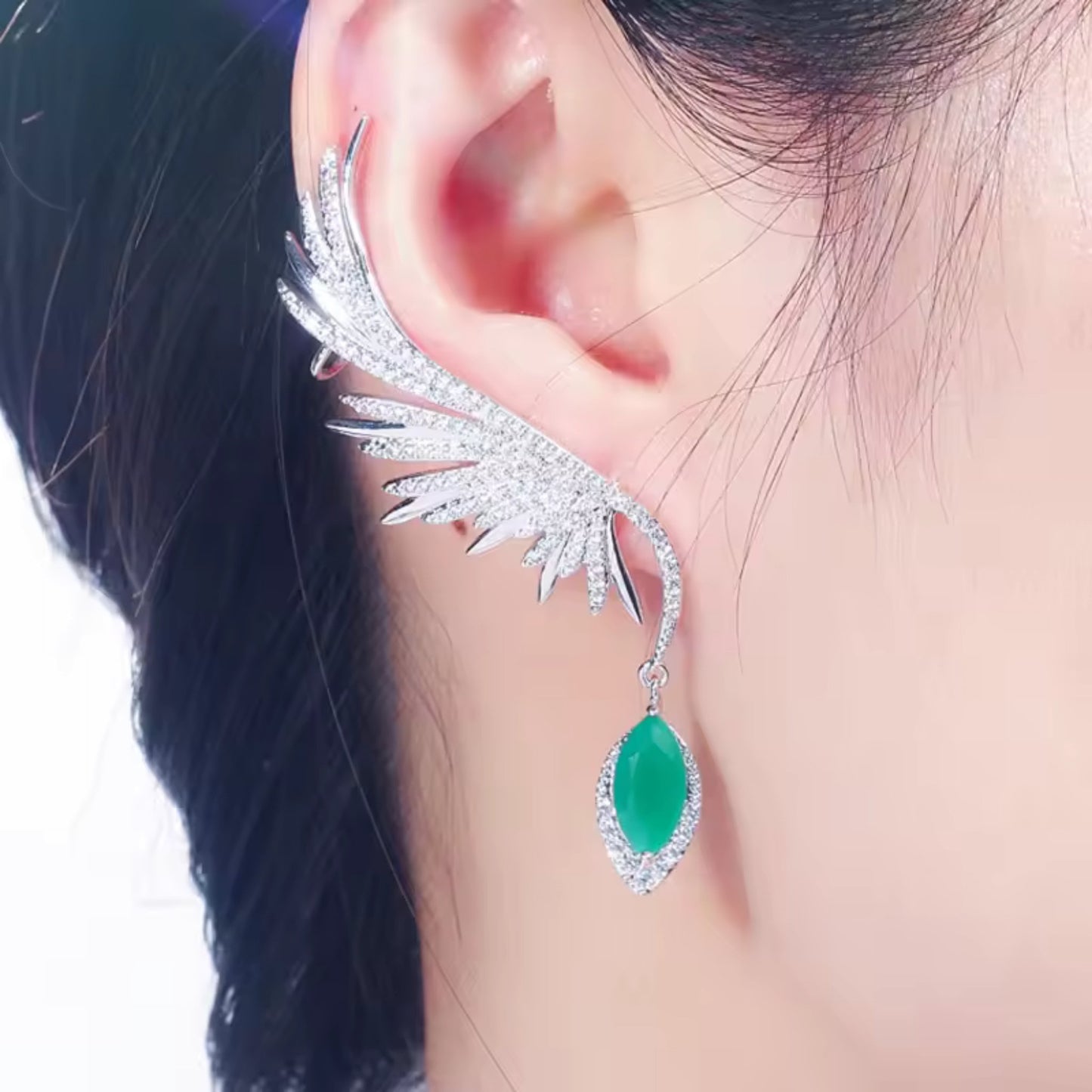 Model wearing Enchanted Wings Feather Drop Earrings, with green zircons cascading along the ear in an elegant climber and drop style.