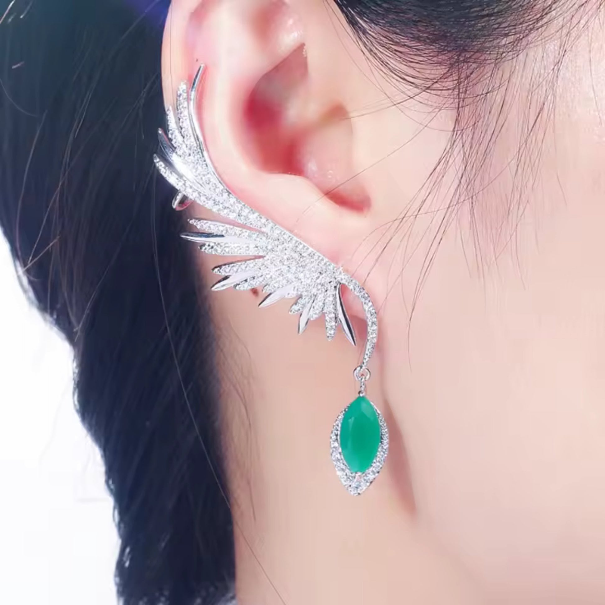 Model wearing Enchanted Wings Feather Drop Earrings, with green zircons cascading along the ear in an elegant climber and drop style.